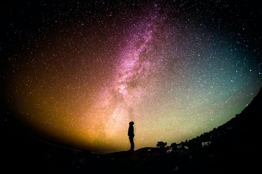The silhouette of a person beneath a multi-colored, starry sky.