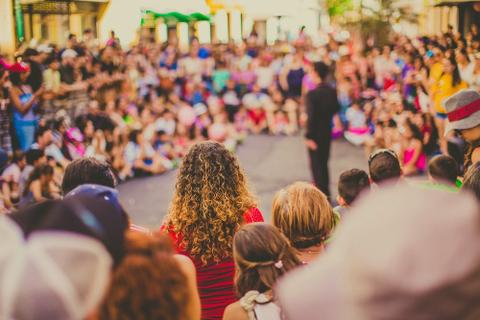 A blurred photo of a crowd of people wearing colorful clothing watching a man.