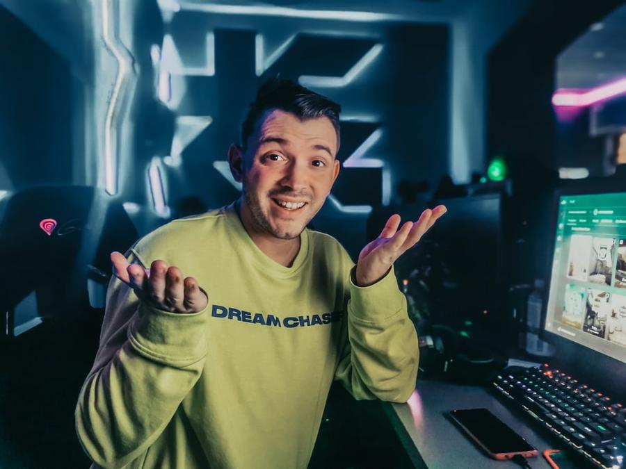 Man in a green sweater shrugging in front of a computer.