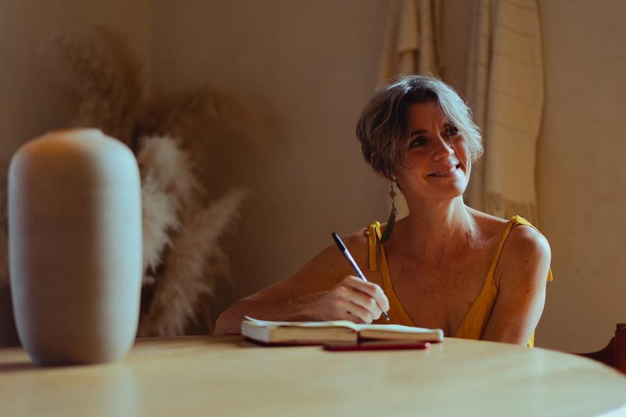 An older author signs a book while smiling at someone off camera.