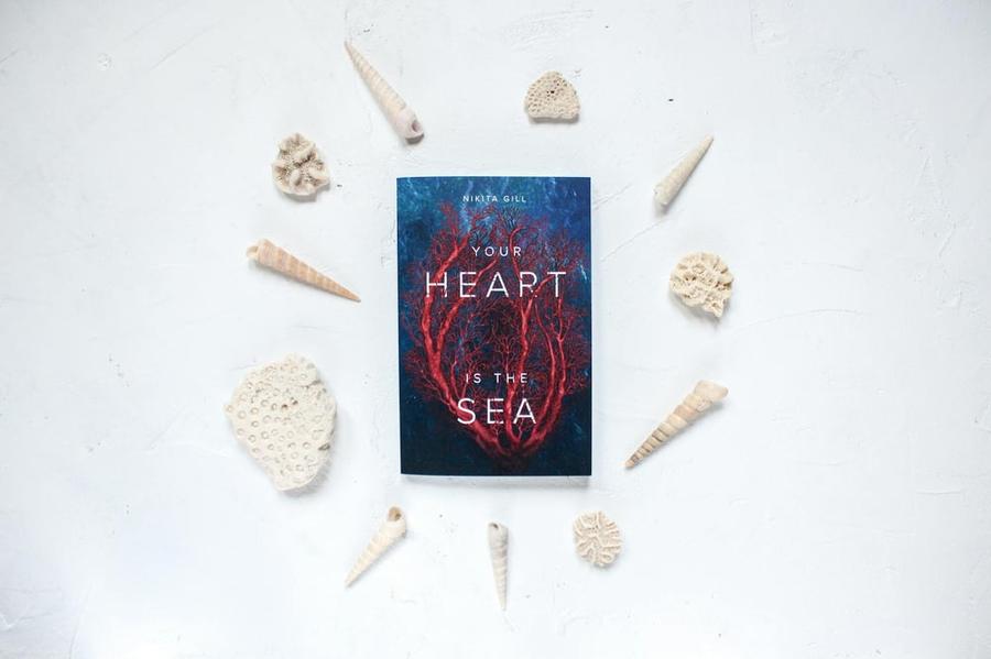 The book Your Heart is the Sea sitting on a white background, surrounded by white seashells.