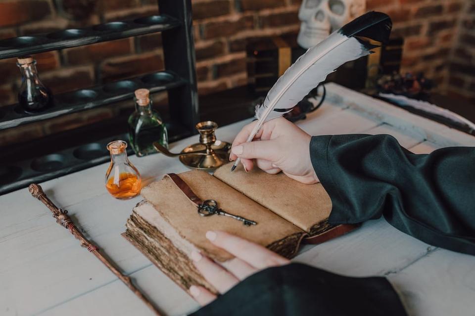 A hand writes in distressed blank book with a big quill.