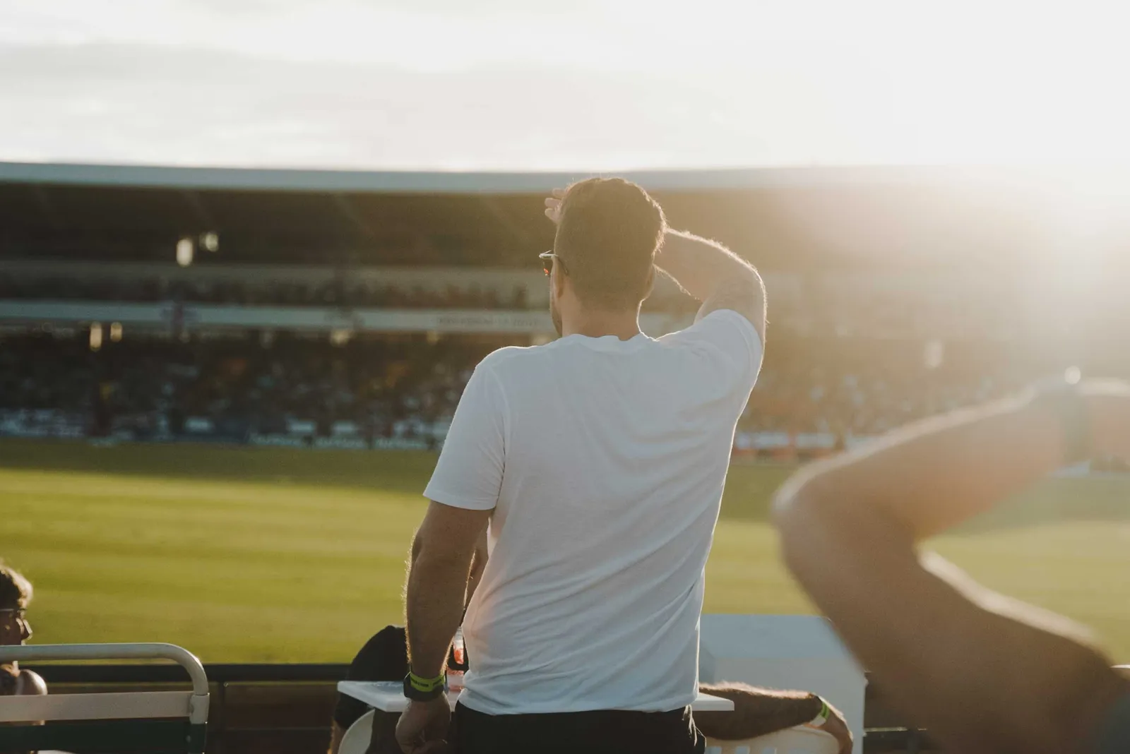 A spectator shields his eyes to follow the cricket, late afternoon.
