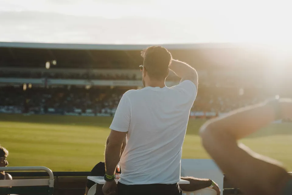 A spectator shields his eyes to follow the cricket, late afternoon.