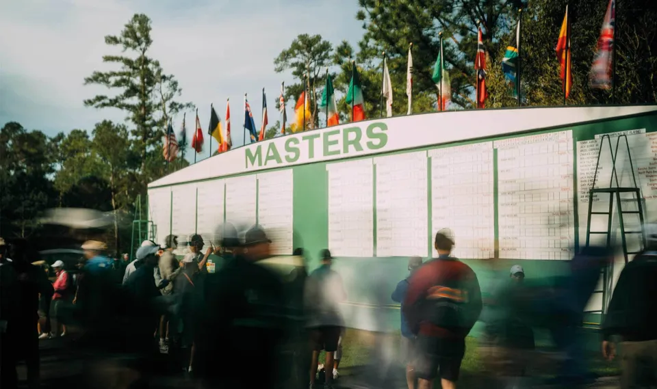 The Masters scoreboard, patrons streaming past.