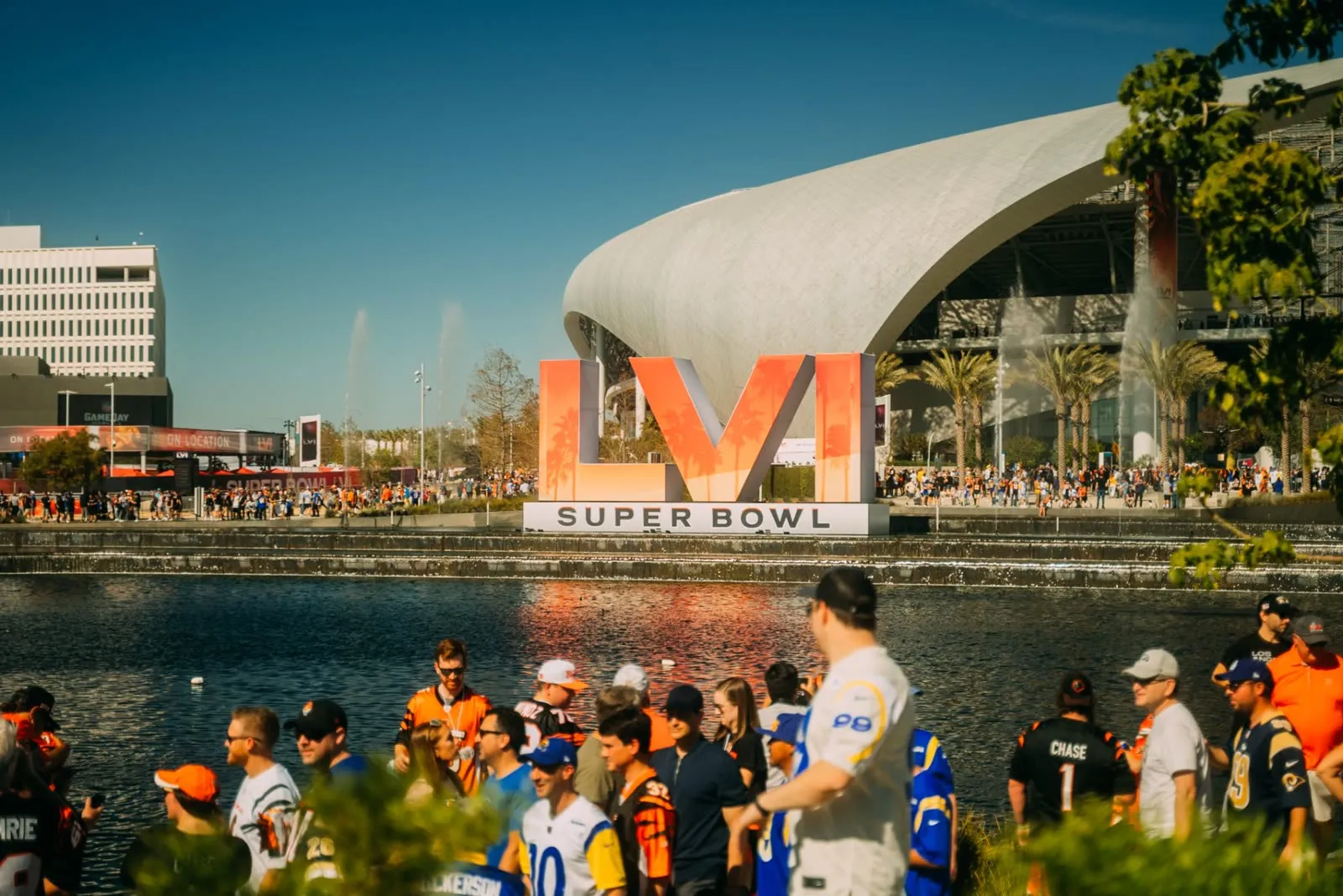 The Super Bowl LVI sign across the lake outside SoFi Stadium, fans gathering in the sunshine.