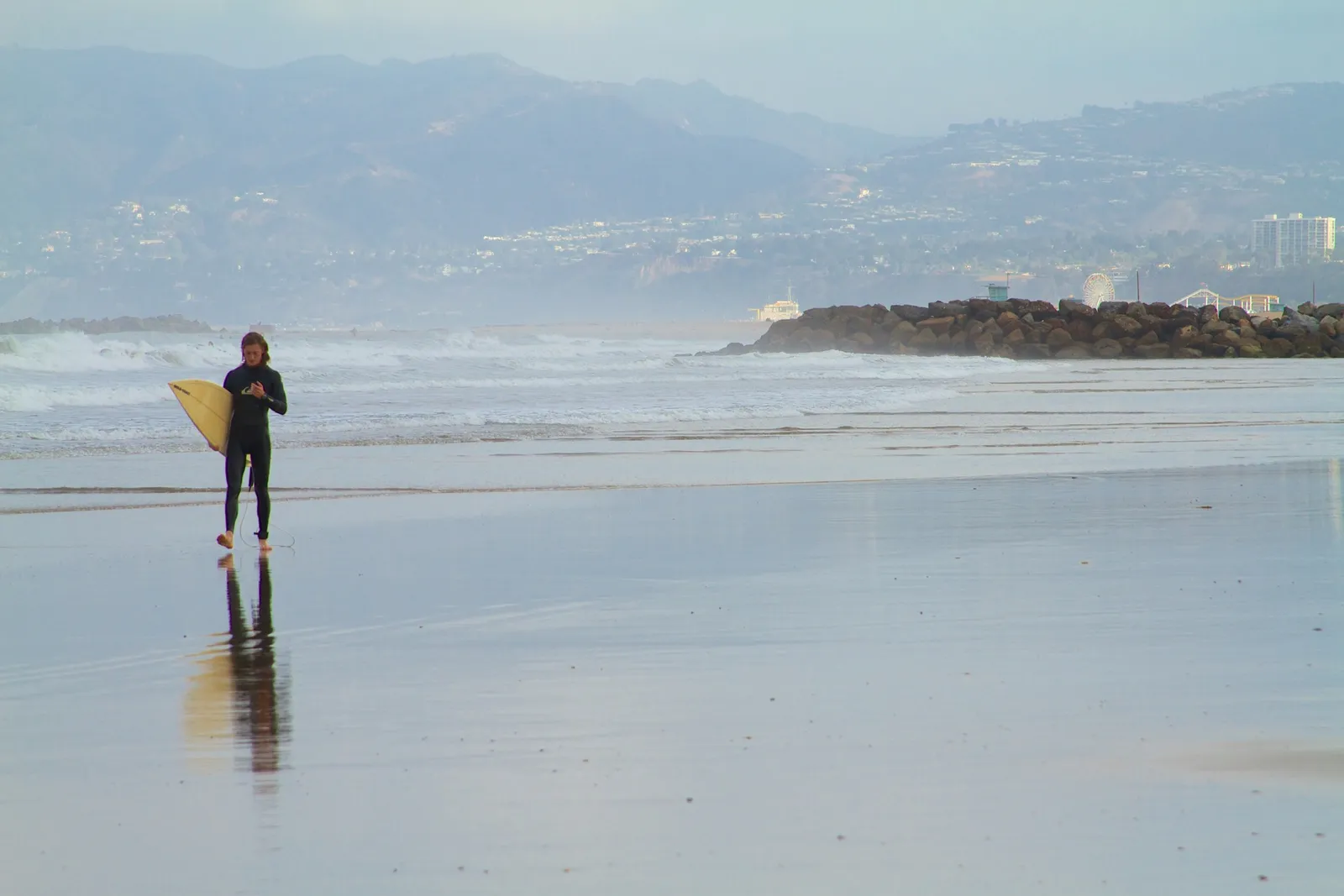 A surfer on a quiet Los Angeles beach at dawn
