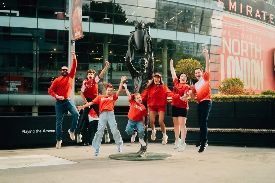 A family jumping for joy at the Wenger statue outside the Emirates Stadium
