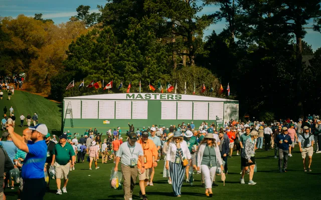 Patrons streaming past the Masters scoreboard in the sunshine.