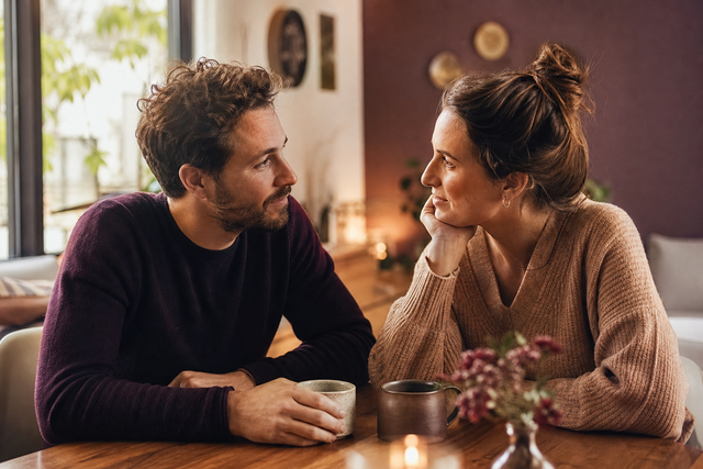 Stel zit warm en aandachtig tegenover elkaar aan tafel tijdens een rustig gesprek