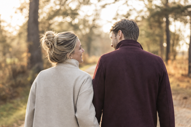 Twee partners die warm naar elkaar glimlachen tijdens een wandeling buiten, van achteren gefotografeerd in zacht daglicht
