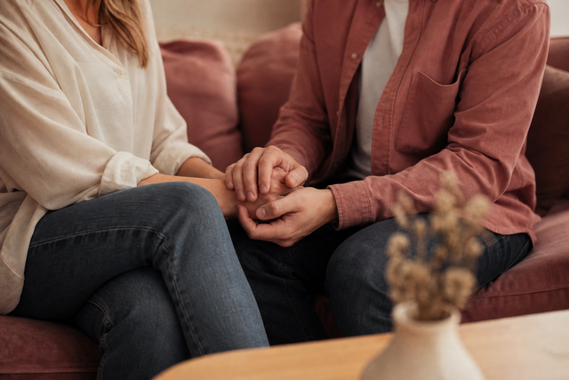 Two partners sit close together on the couch holding hands after a conversation