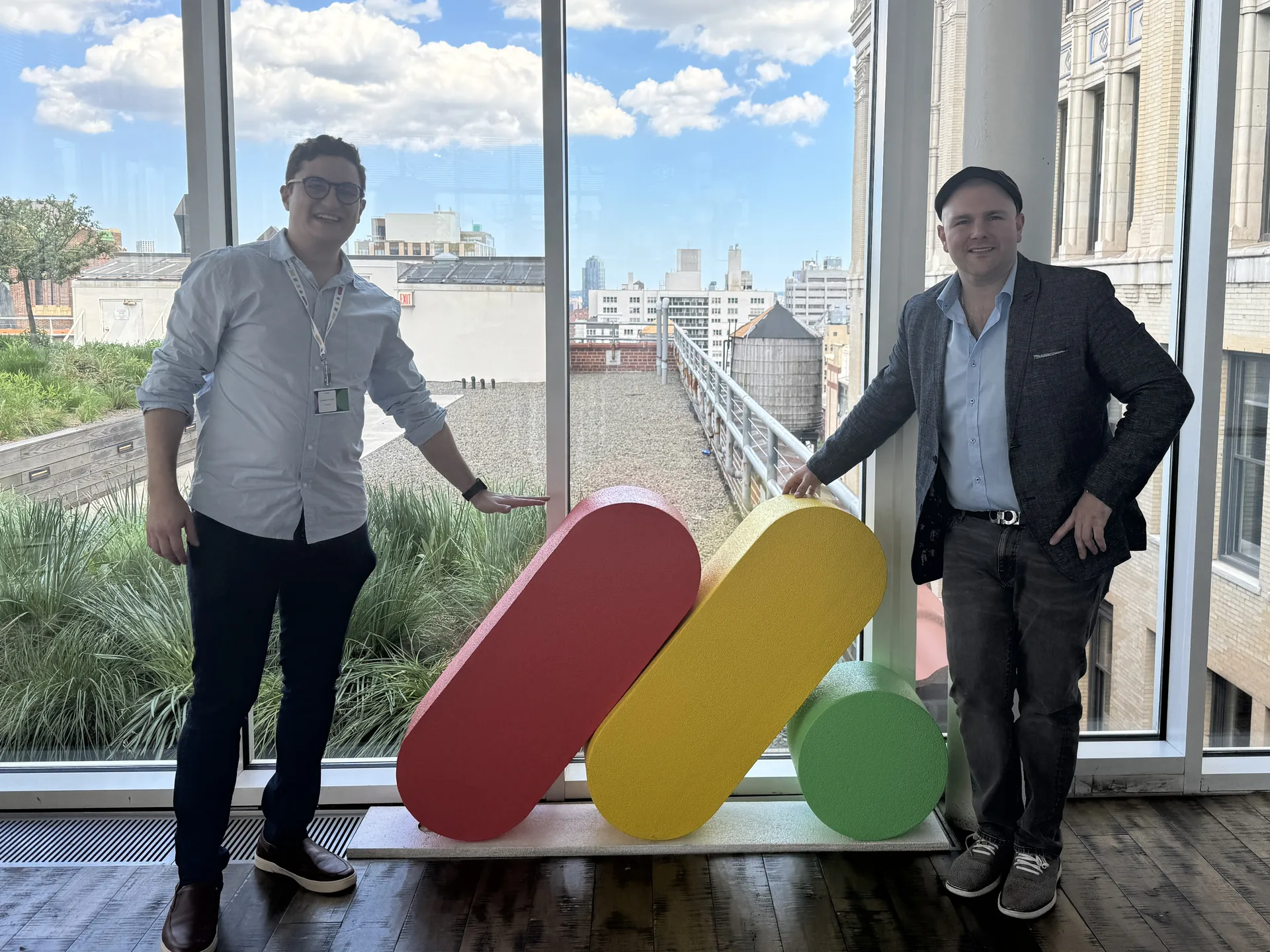 The two founders of Worktables beside the monday.com logo sculpture at the monday.com office