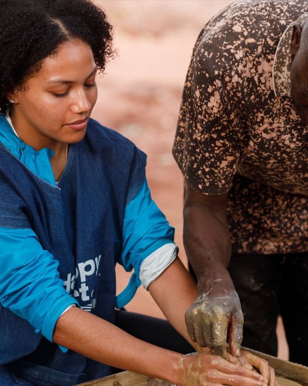 A potter guiding a guest\u2019s hands on the wheel