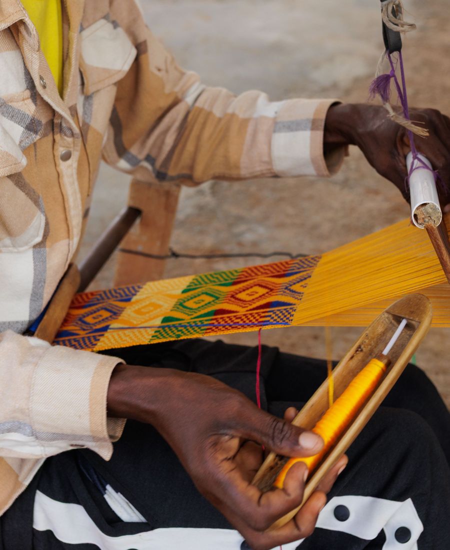 Hands weaving kente on a loom at Adanwomase