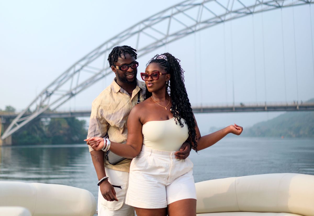 A couple on the boat deck with the Adomi Bridge behind them