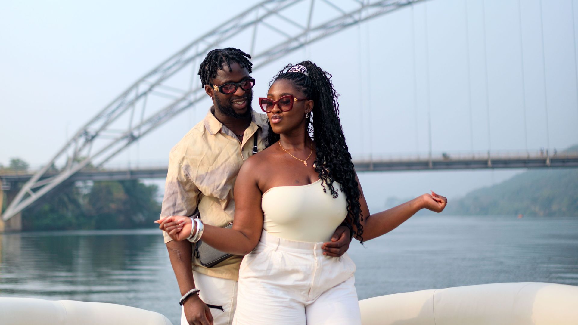 A couple on the boat deck with the Adomi Bridge behind them