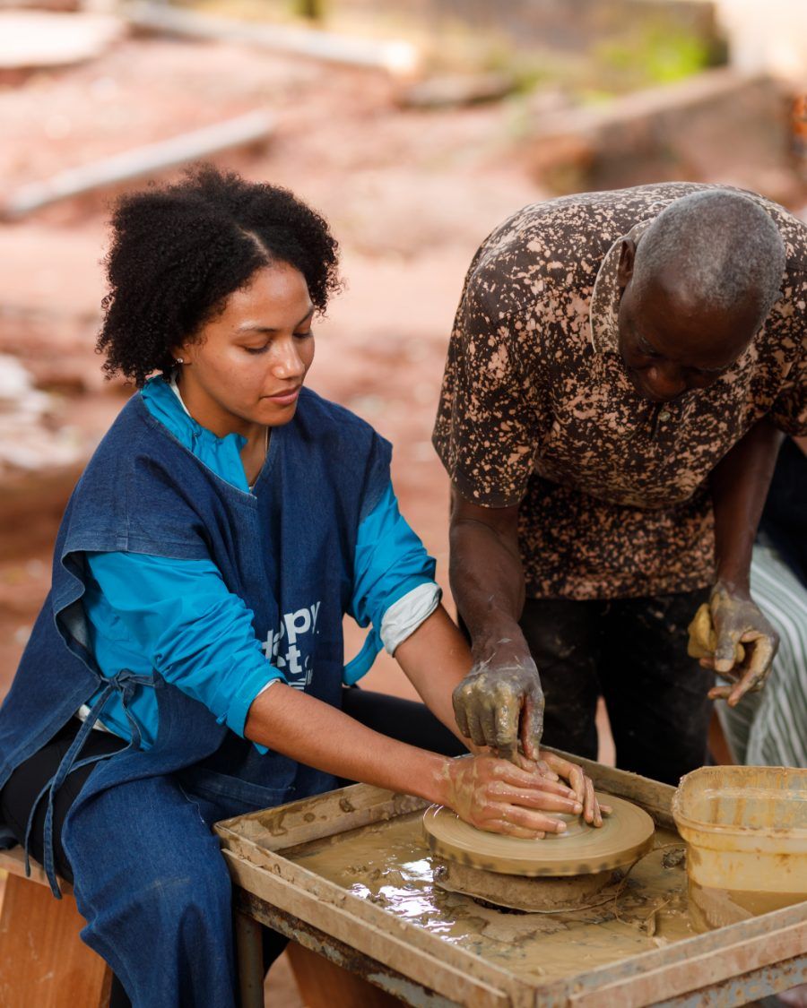 A guest at the potter's wheel with a Ghanaian potter guiding her hands on the clay