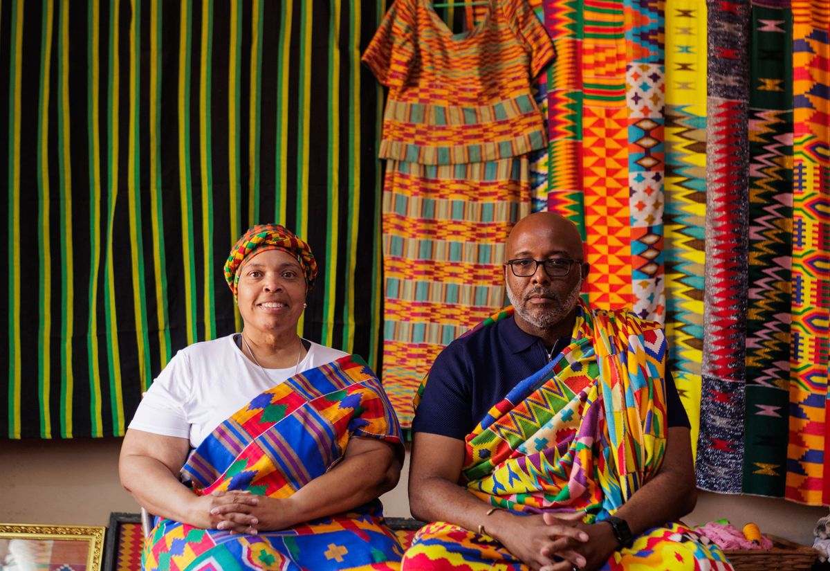 A couple seated in kente cloth in front of a weaver’s stall near Kumasi