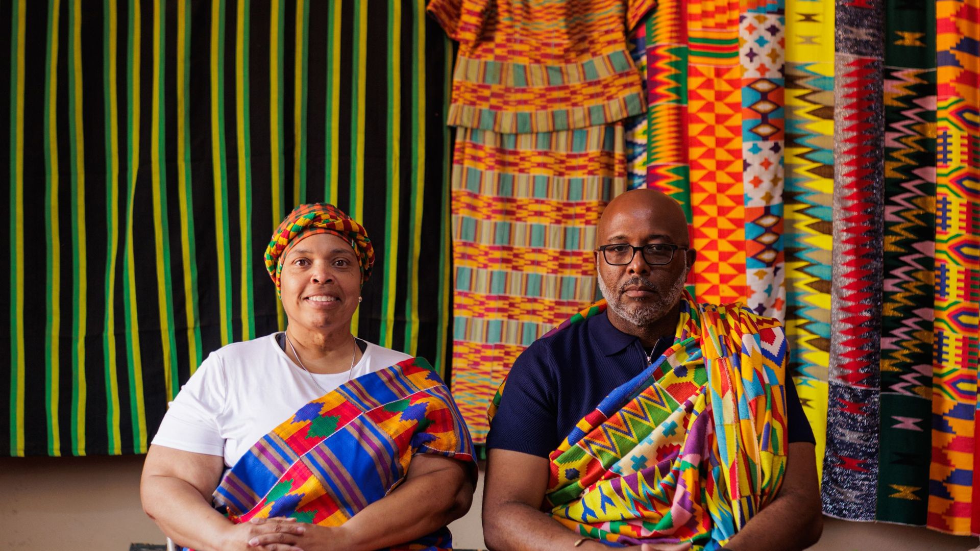 A couple seated in kente cloth in front of a weaver’s stall near Kumasi