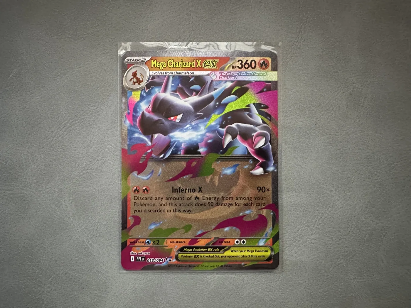 Een Mega Charizard X ex kaart in een penny sleeve: een dun, doorzichtig hoesje dat bovenaan net iets boven de kaart uitsteekt.