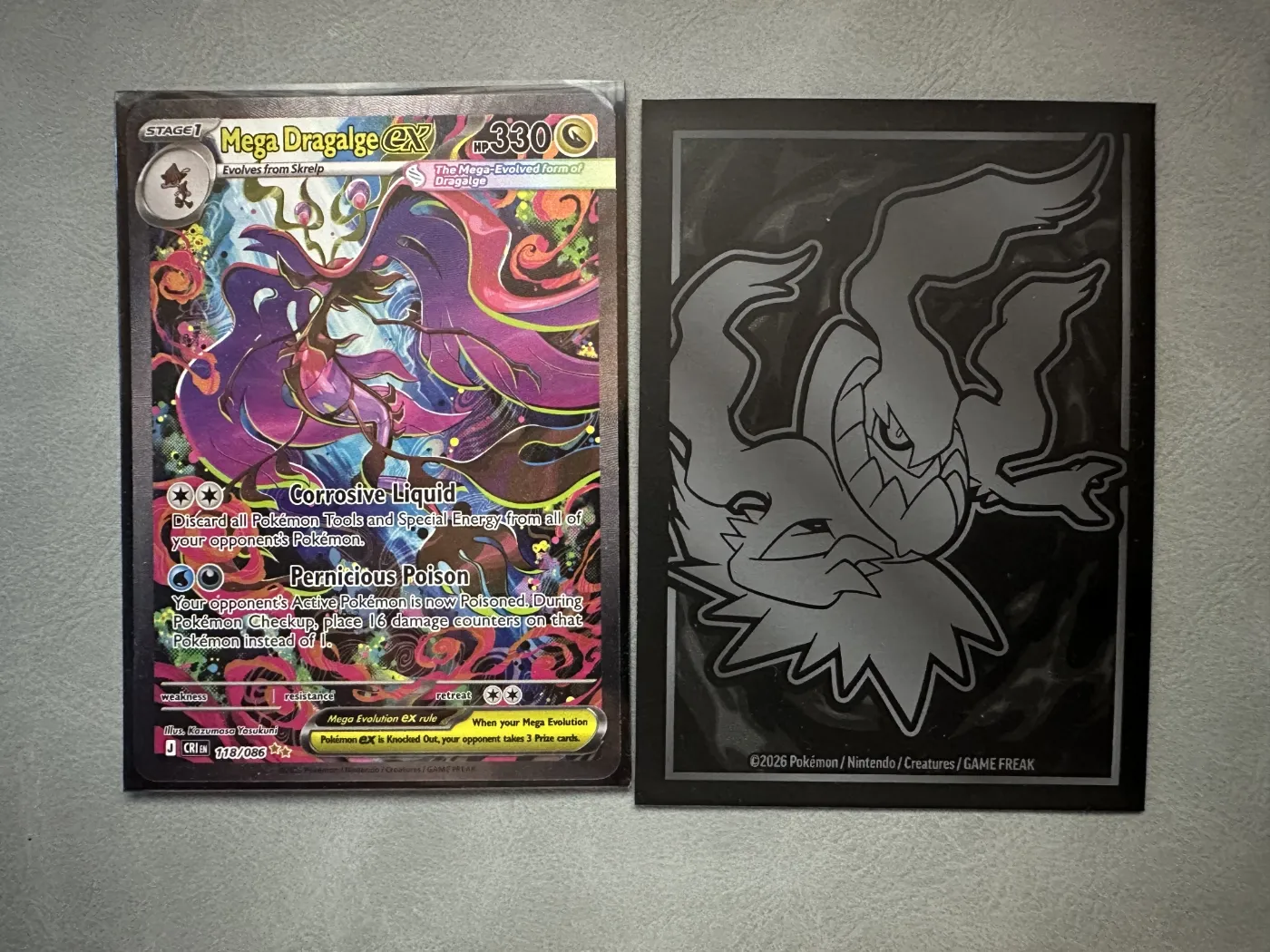 Een deck sleeve uit de Pitch Black Elite Trainer Box. Links een Mega Dragalge ex kaart in de sleeve, rechts de zwarte achterkant met een illustratie uit de set. De voorkant is doorzichtig, de achterkant niet.
