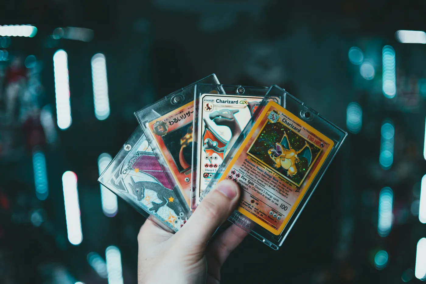 Een hand met vier Charizard-kaarten uit verschillende Pokémon-sets in toploaders.
