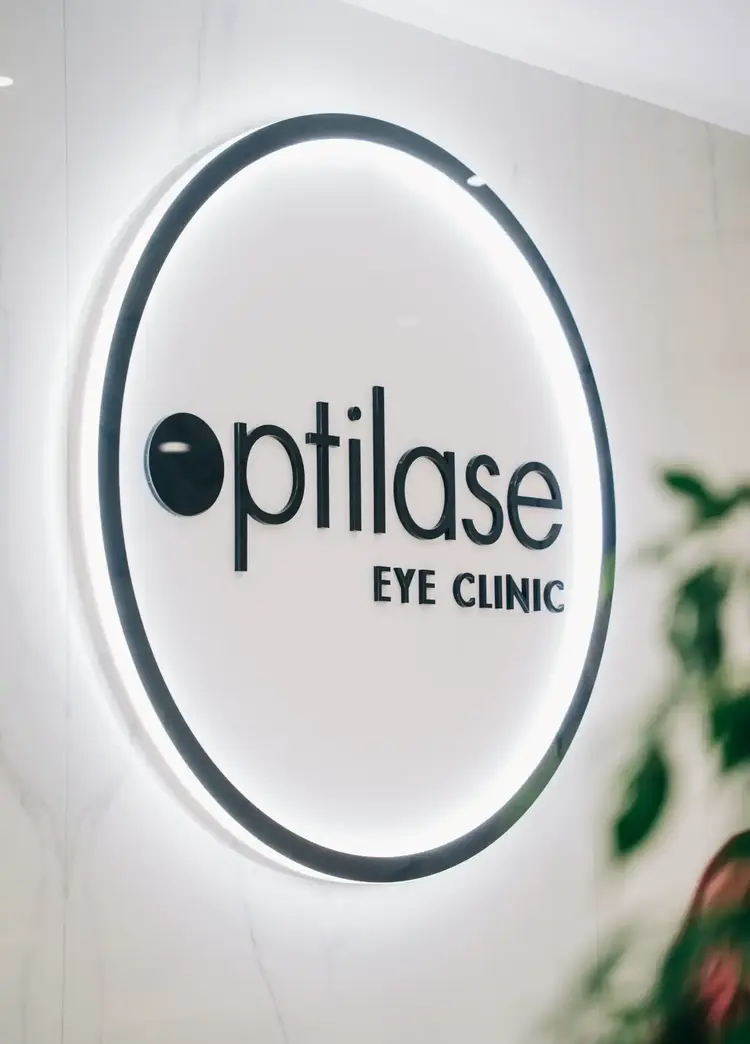 Illuminated Optilase Eye Clinic logo sign on a white wall