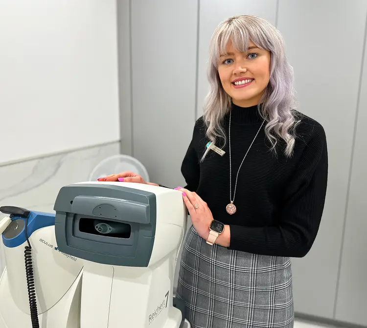 Smiling young woman beside an Oculus eye examination device at Optilase
