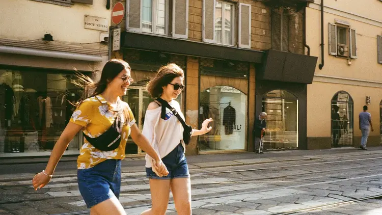 Two women laughing as they cross a sunlit city street