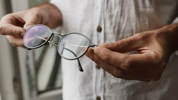 Pair of hands holding up a pair of round reading glasses