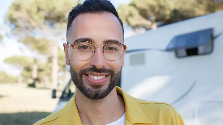 Smiling bearded man wearing round glasses outdoors on a sunny day