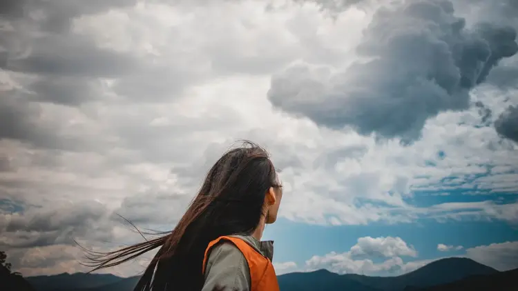 Woman looking up at a sky of heavy grey and white clouds