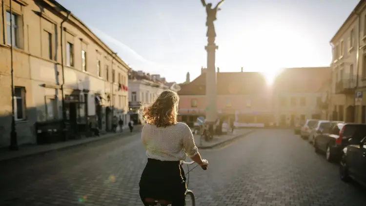 Woman cycling through a cobbled square towards the low evening sun