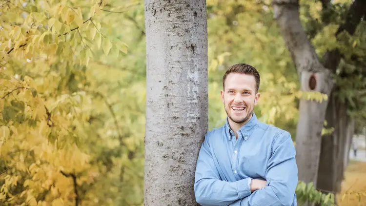 Man with folded arms leaning against a tree in an autumn park