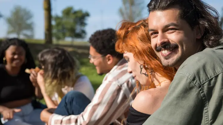 Man smiling over his shoulder while sitting outdoors with friends