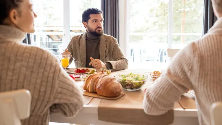 Family sharing a table of bread, salad and juice by a window