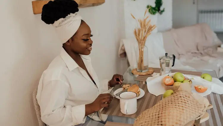 Woman eating a breakfast of fruit and pastries at a table at home