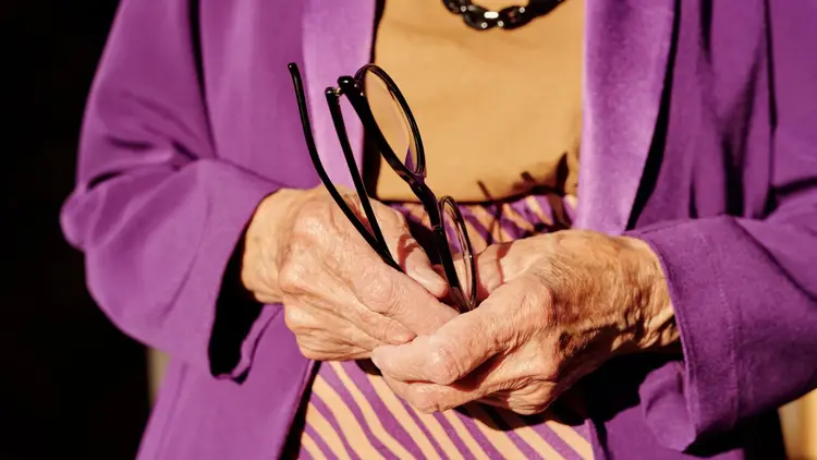 Older woman's hands holding a folded pair of reading glasses