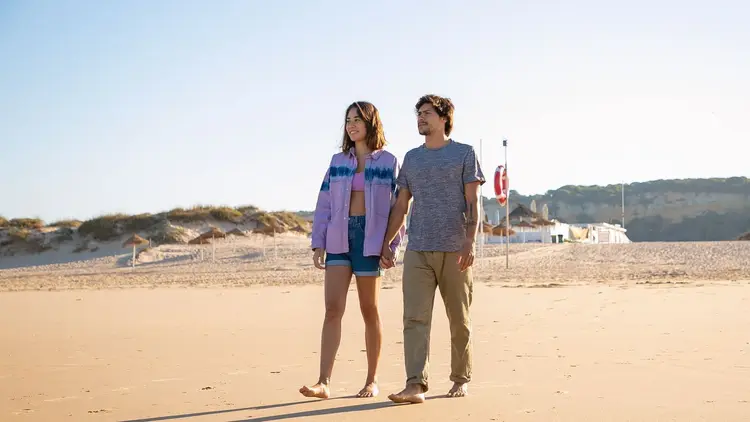 Couple walking together across a wide sandy beach in the sunshine