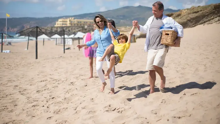 Parents swinging a child between them as they walk along a beach