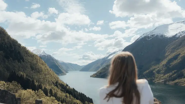 Woman looking out over a fjord framed by snow-capped mountains
