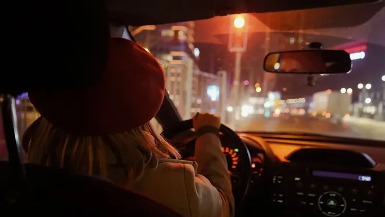 View from inside a car of a driver at night, city lights blurred ahead