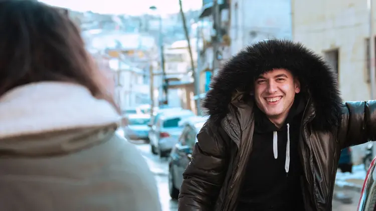 Man in a fur-hooded coat laughing with a friend on a winter street