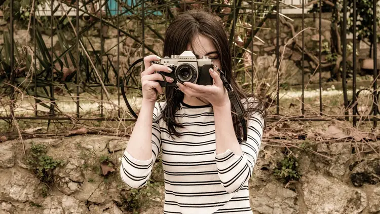 Young woman raising a film camera to her eye to take a photograph