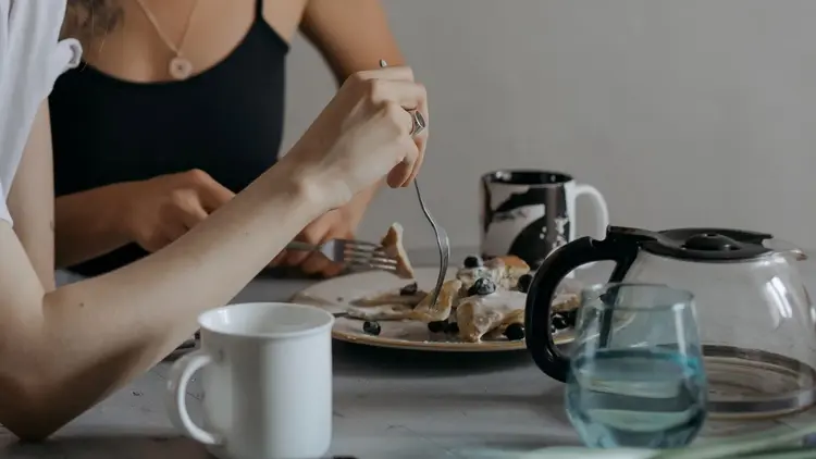 Person eating a plate of food at a table set with coffee and water