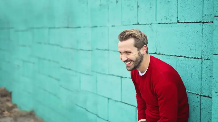 Man in a red jumper laughing in front of a painted teal wall