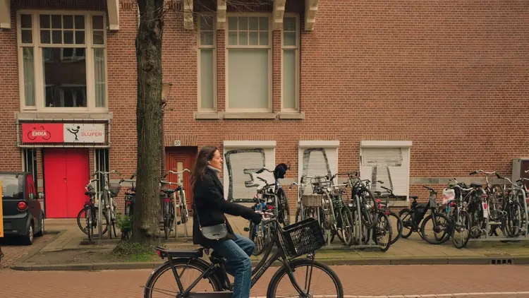Woman cycling past rows of parked bicycles on a city street