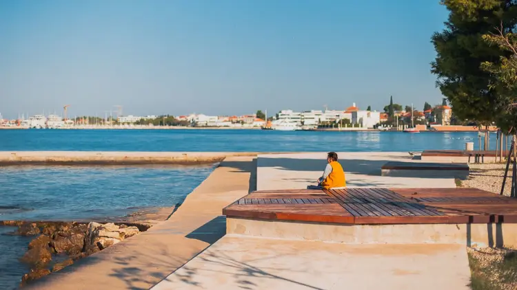 Person sitting alone on a waterfront deck looking out over calm water