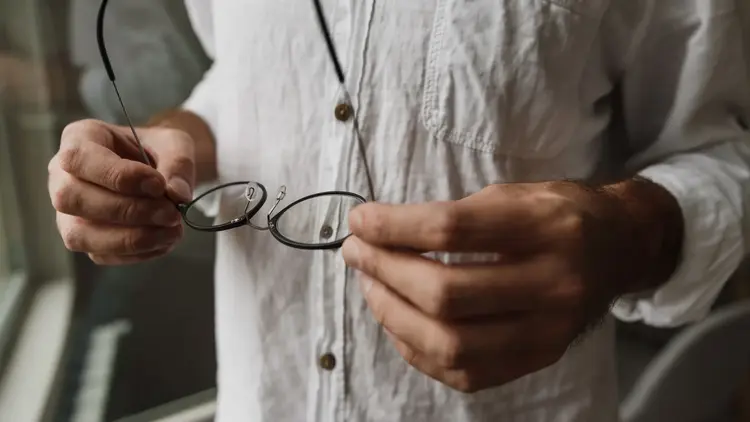 Man holding a pair of glasses in both hands in front of a linen shirt